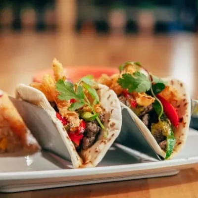 Three soft-shelled tacos with grilled meat, peppers, onions, and cilantro.