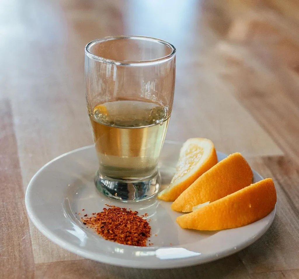 Amber drink with orange wedges and spice on a wooden table.