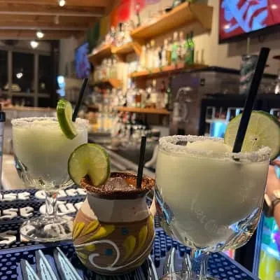 Three drinks on a bar: two margaritas, one in a clay cup.