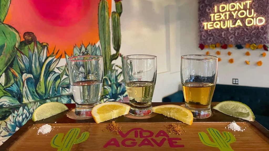 Wooden tray with three tequila shots, citrus, salt, and desert mural.