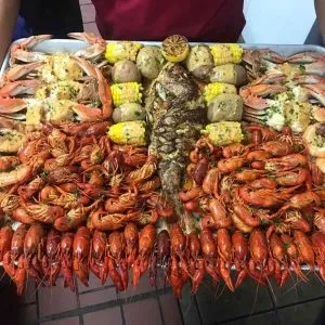 Overflowing metal tray of seafood boil with crawfish, crabs, and fish.