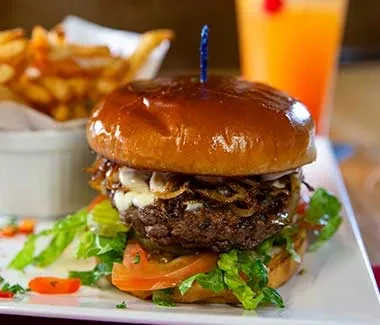 Close-up gourmet burger, fries, and orange drink on a white plate.