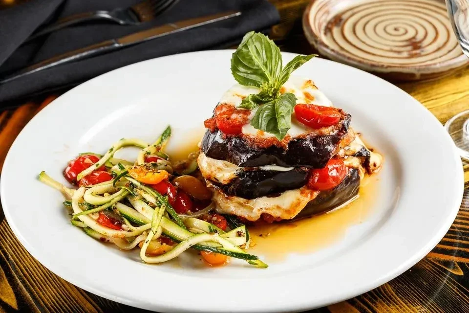 Layered eggplant with melted cheese, tomatoes, basil, and zucchini noodles.