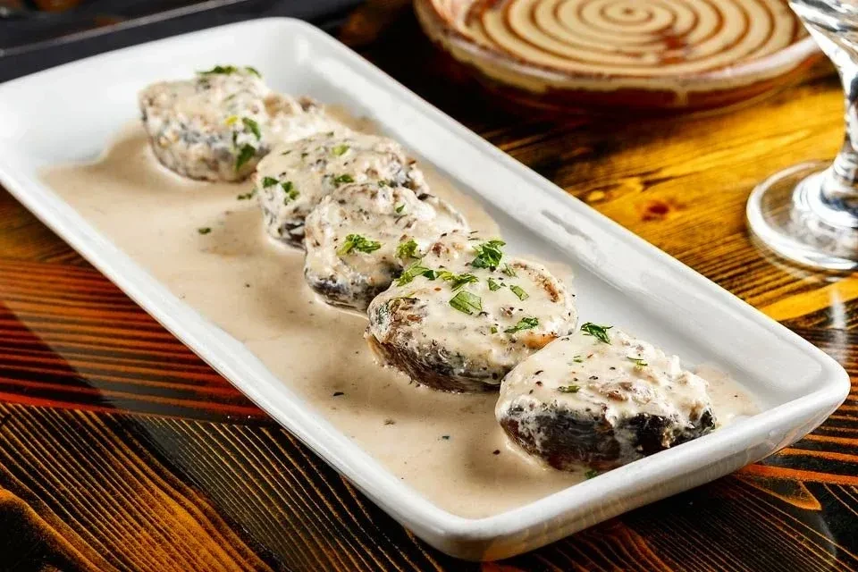 Five creamy, herb-topped items on a white plate, wooden table.