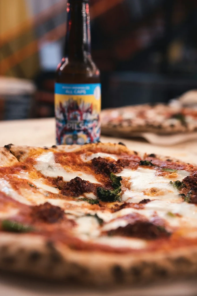 Close-up of fresh Neapolitan pizza with meat, cheese, herbs, and beer.