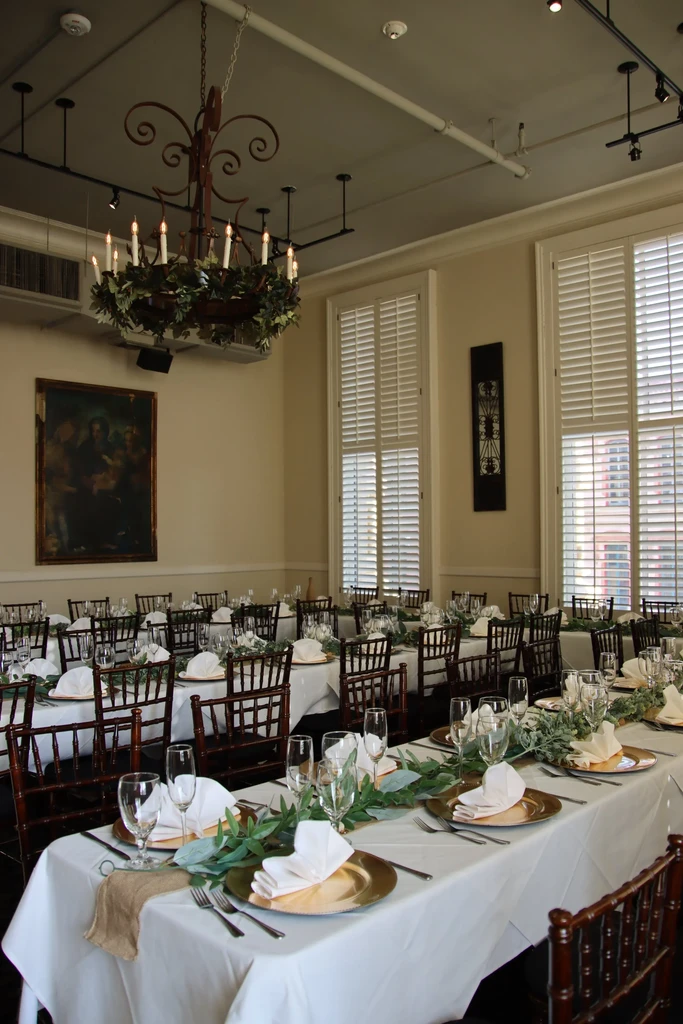 Elegant formal dining room prepared for an event, featuring greenery and chandelier.