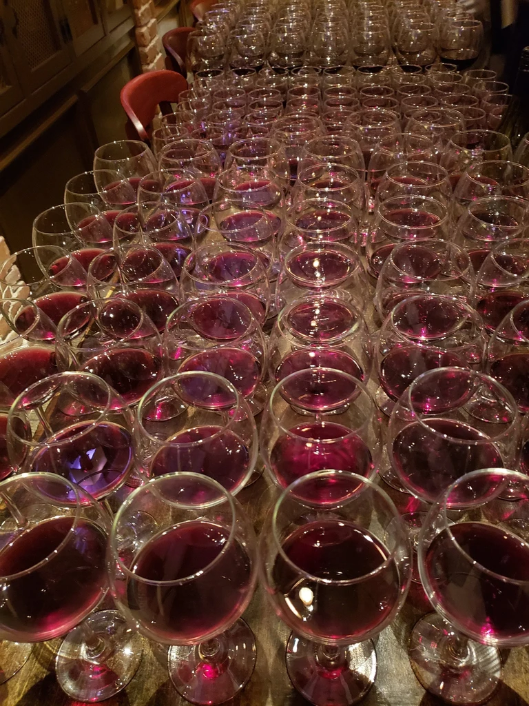 Neat rows of hundreds of red wine glasses on a wooden table.