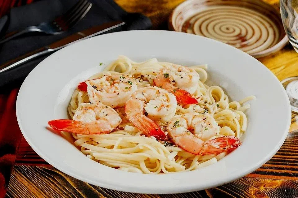 Shrimp pasta in a white bowl, garnished with green herbs.
