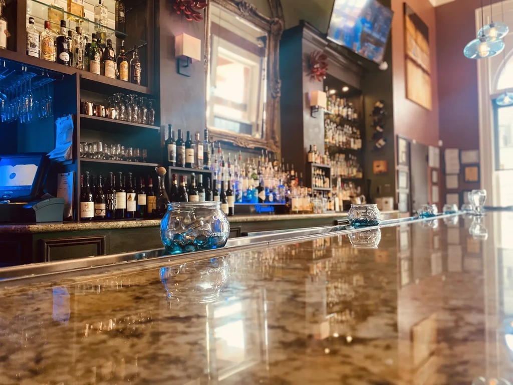 Empty bar with reflective counter, extensive shelves of bottles and glassware.