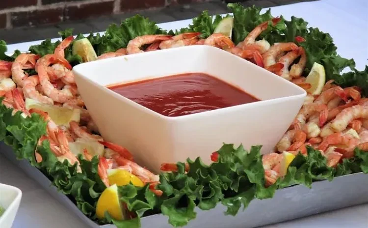 Platter of shrimp cocktail with central sauce, lettuce, and lemons.