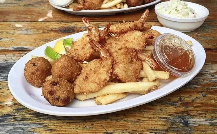 Close-up of fried shrimp, fries, hushpuppies, sauce, and lime on plate.