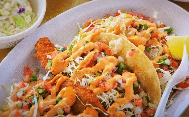 Two fish tacos with crispy fish, orange sauce, and lime.