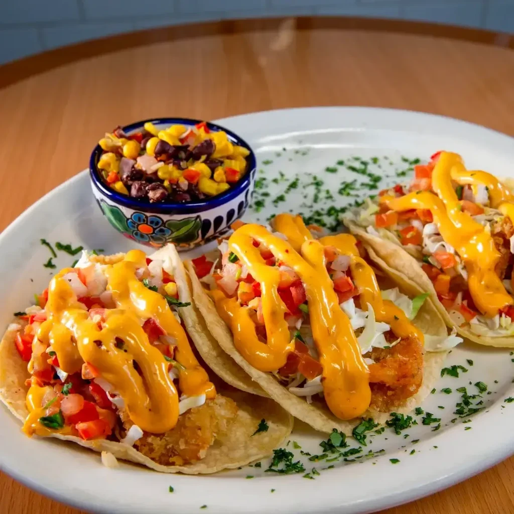 Three crispy fish tacos with pico de gallo, sauce, and corn salsa.