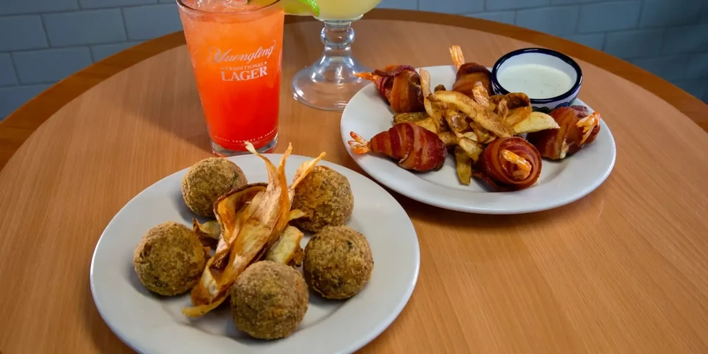 Restaurant table with fried appetizers, shrimp, fries, and two drinks.