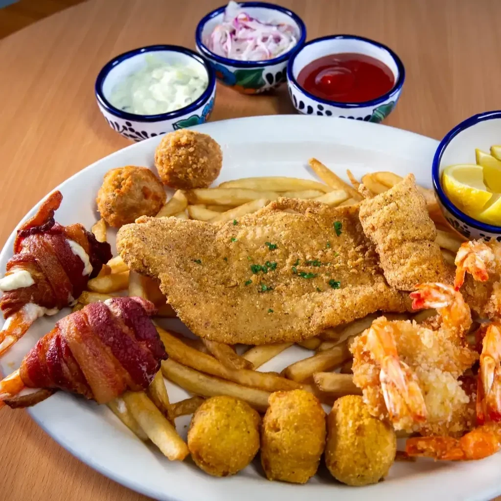 Fried seafood platter with fish, shrimp, french fries, and hush puppies.