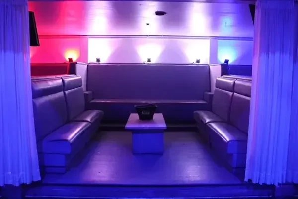 U-shaped VIP booth with plush seating, table, and colorful club lighting.