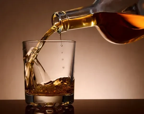 Amber spirit pours from bottle into glass, creating a splash.