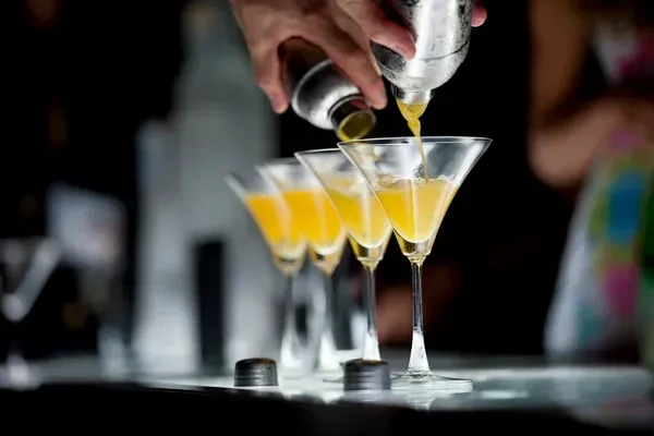 Close-up of bartender pouring yellow liquid into martini glasses.