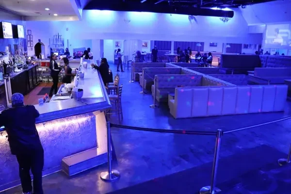 Modern bar interior with strong blue lighting, booth seating, and patrons.