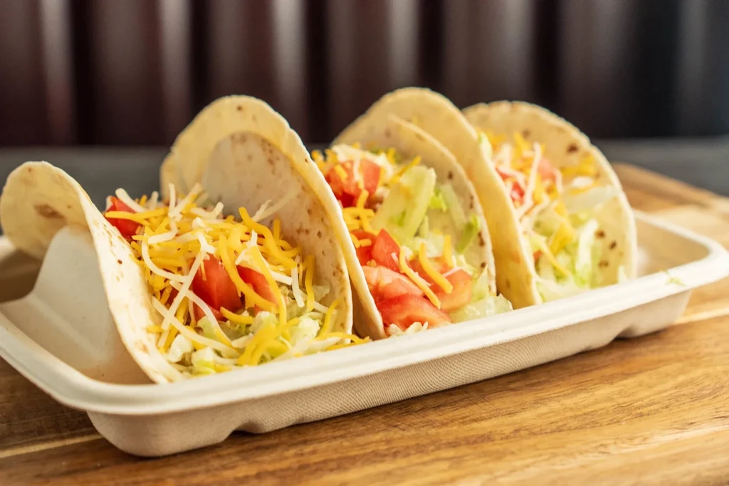 Three soft flour tacos with lettuce, tomatoes, and cheese in a tray.