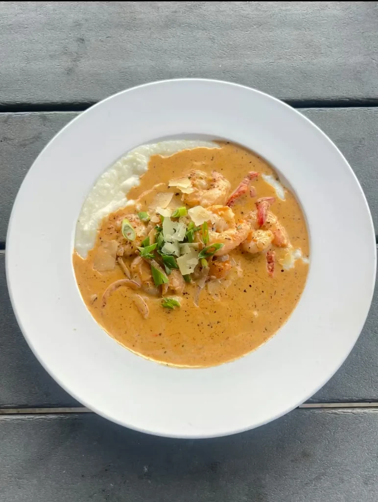 Shrimp and grits in white bowl, topped with green onions and cheese.