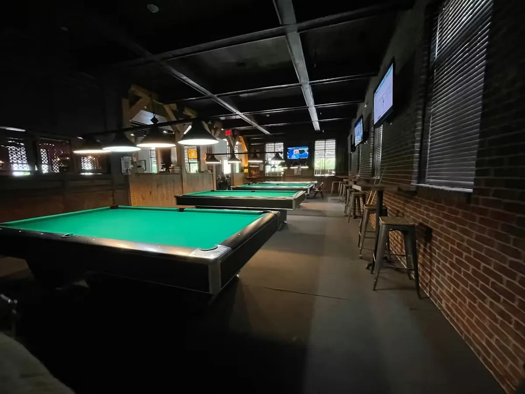 Dim pool hall interior featuring green billiard tables and exposed brick.
