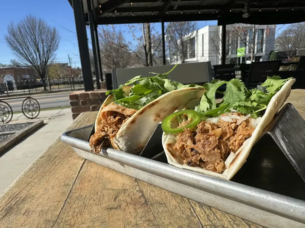 Two pork tacos with cilantro, onions, jalapeños on a wooden table.