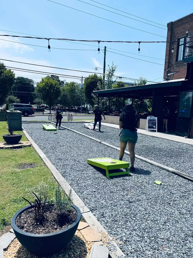 Outdoor restaurant guests play cornhole on a gravel court.