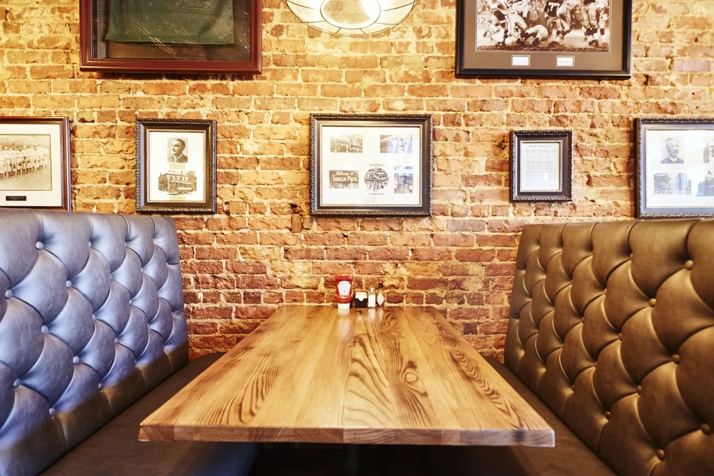 Restaurant booth: empty wooden table, tufted benches, brick wall, condiments.