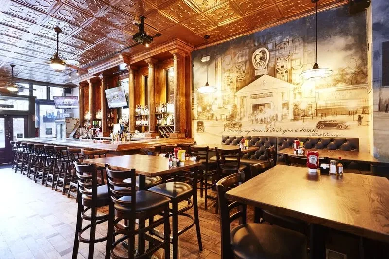 Restaurant interior with wooden bar, city mural, and embossed copper ceiling.