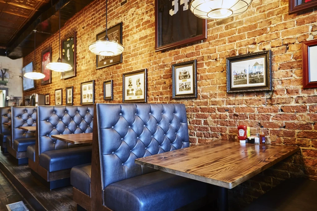Empty restaurant with navy tufted booths, red brick wall, framed art.