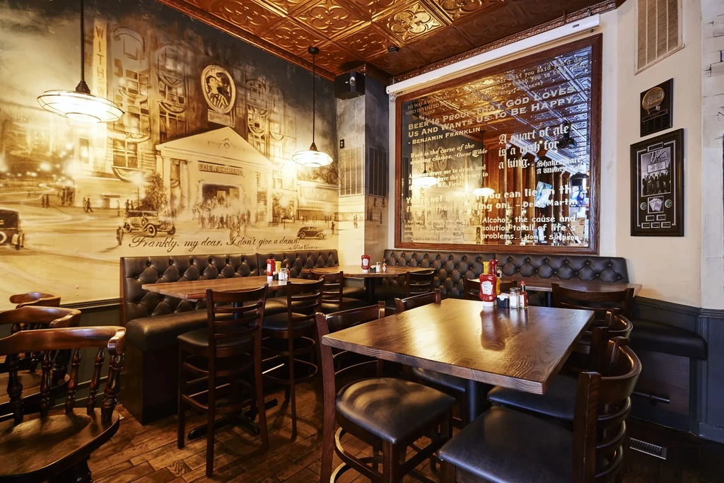 Vintage pub interior with leather seating, mural, and embossed ceiling tiles.