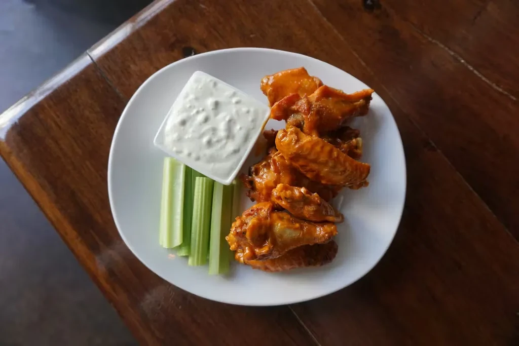 Buffalo wings, creamy dip, and green celery on a plate.