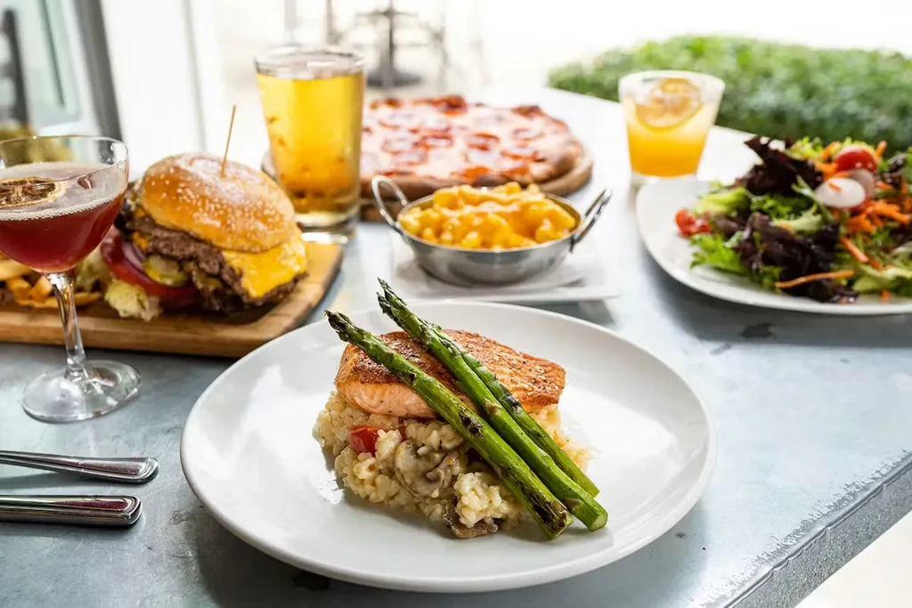 Table spread of salmon, cheeseburger, pizza, macaroni and cheese, and salad.