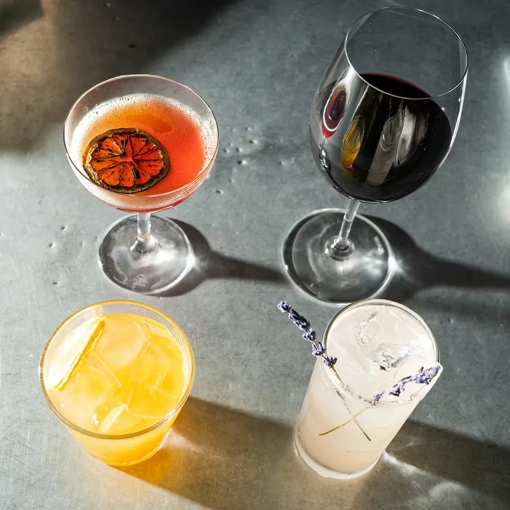 Overhead shot of four distinct, garnished alcoholic drinks on a metal surface.