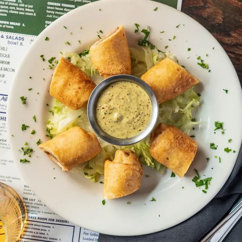 Six fried appetizers, dipping sauce, and lettuce on a white plate.