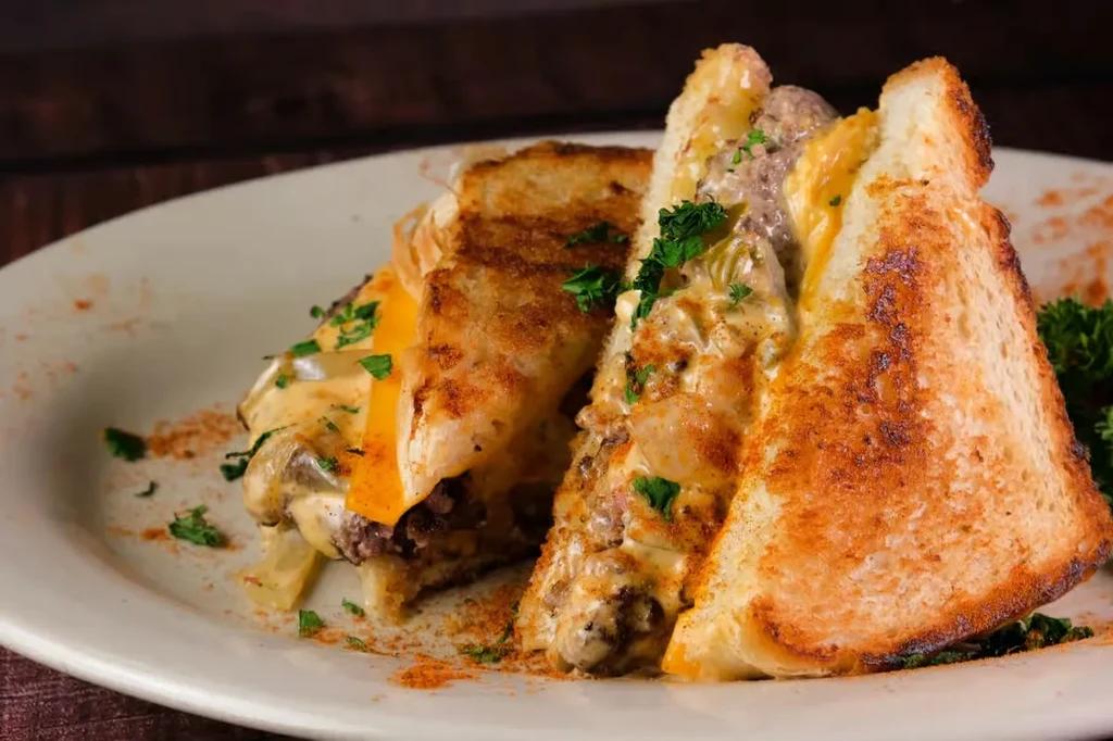 Grilled sandwich cut in half, with meat, melted cheese, onions, and herbs.