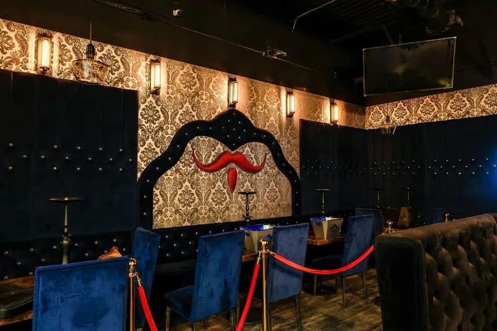Ornate shisha lounge with tufted velvet booths and a red mustache.