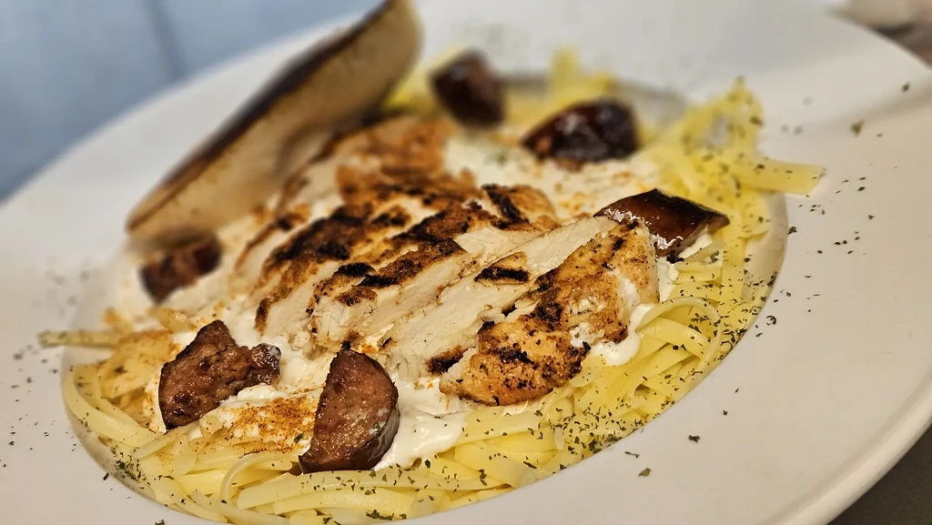 Creamy pasta with grilled chicken, dark chunks, and green herbs.