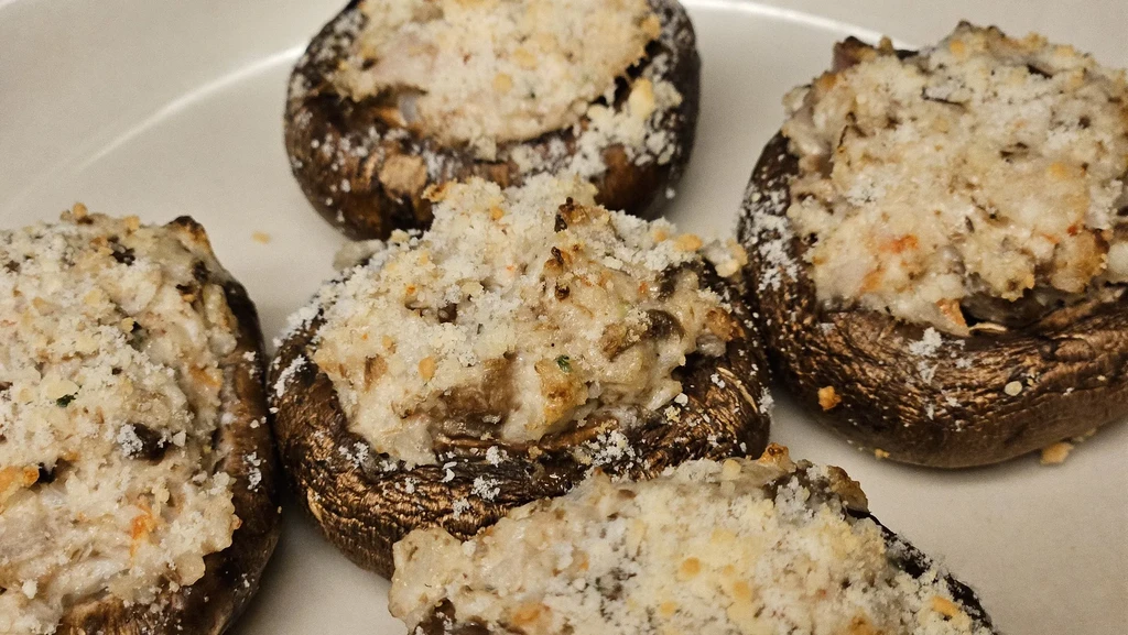 Close-up of five stuffed mushrooms with savory topping on a white plate.