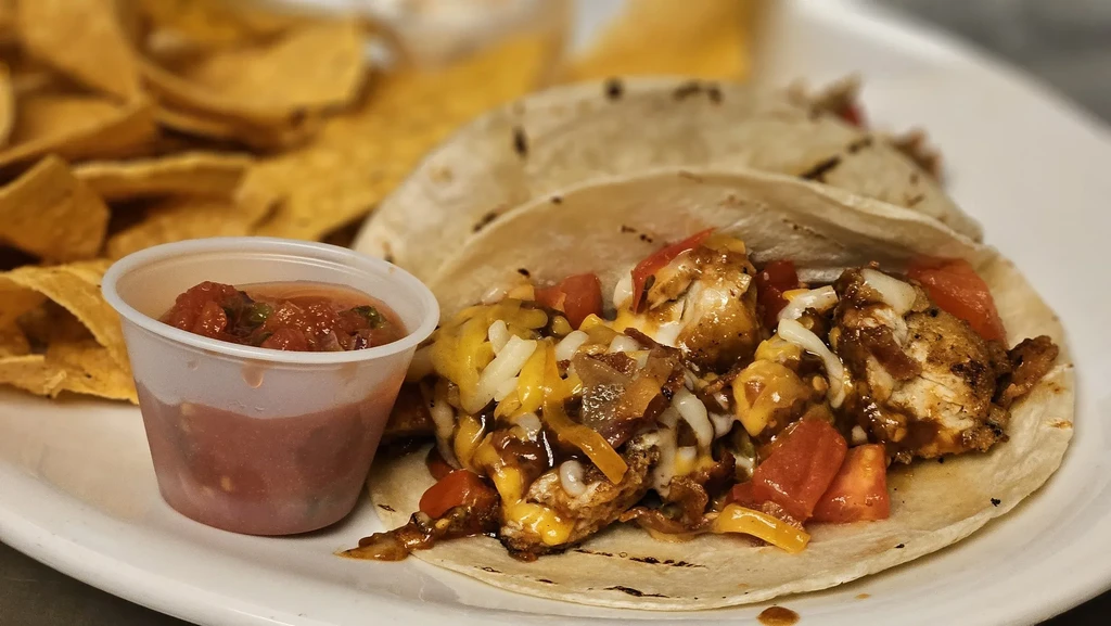 Two chicken soft tacos with salsa and tortilla chips.