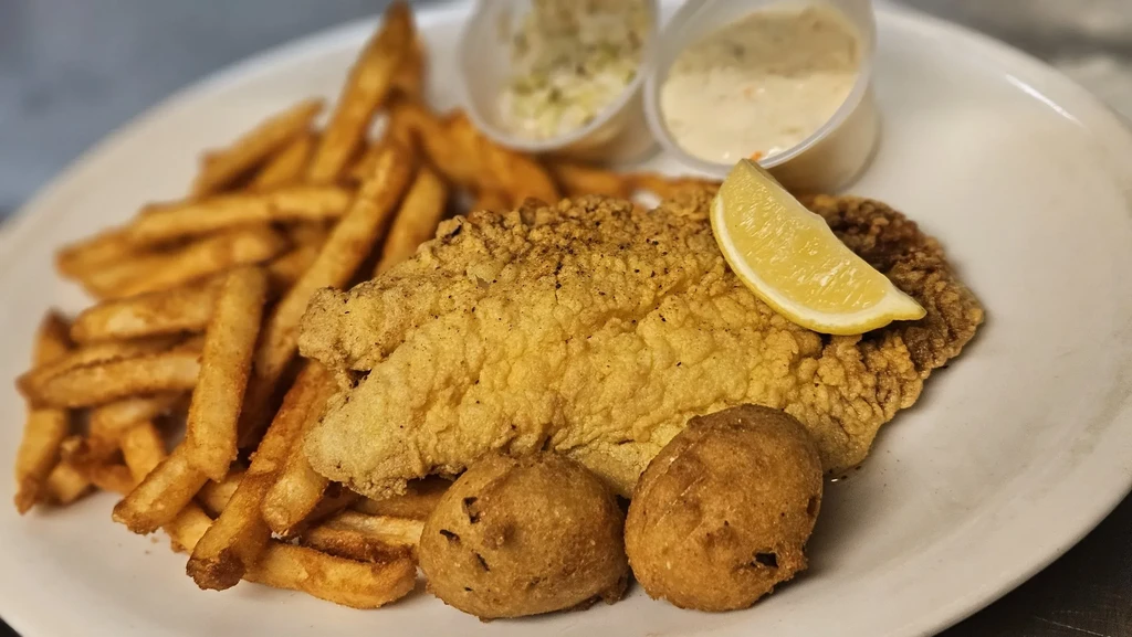 Plate of fried fish, fries, hushpuppies, lemon, coleslaw, and tartar sauce.