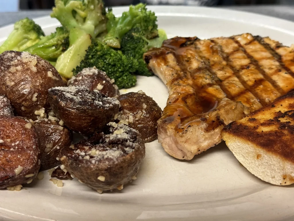 Plated meal with grilled meat, roasted potatoes, broccoli, and toasted bread.