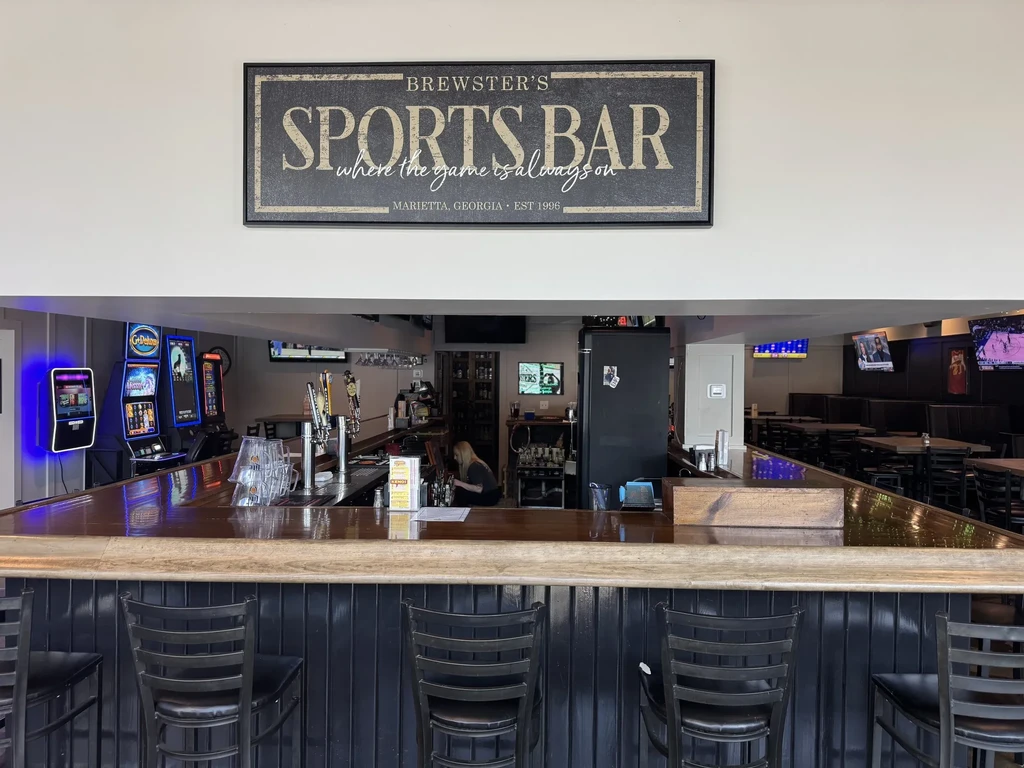 Interior of Brewster's Sports Bar with sign, bar, and TVs displaying sports.