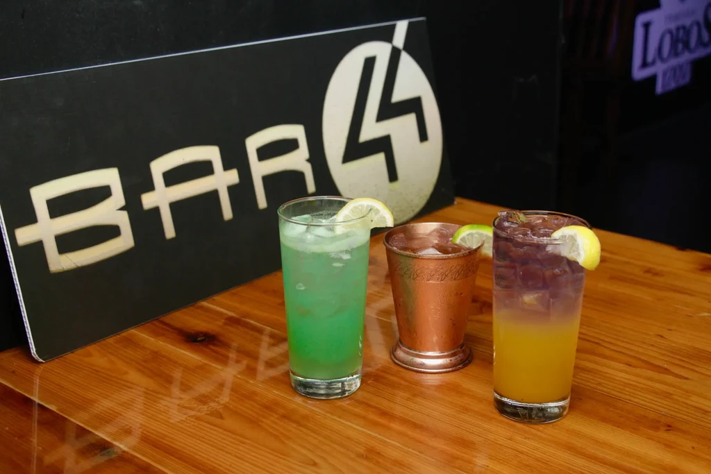 Three colorful drinks on a bar with "BAR 44" sign.
