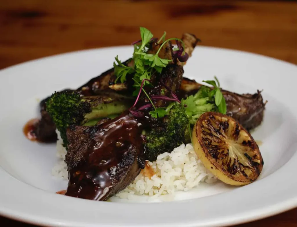 Dish of sauced meat, white rice, broccoli, and charred lemon.