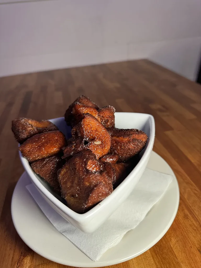 White bowl of glossy fried sweet plantains on a wooden table.