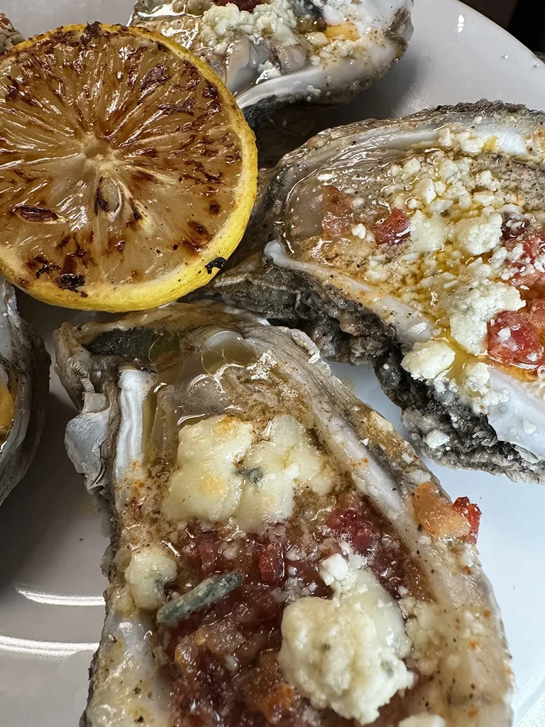 Roasted oysters with red topping, white cheese, and grilled lemon.