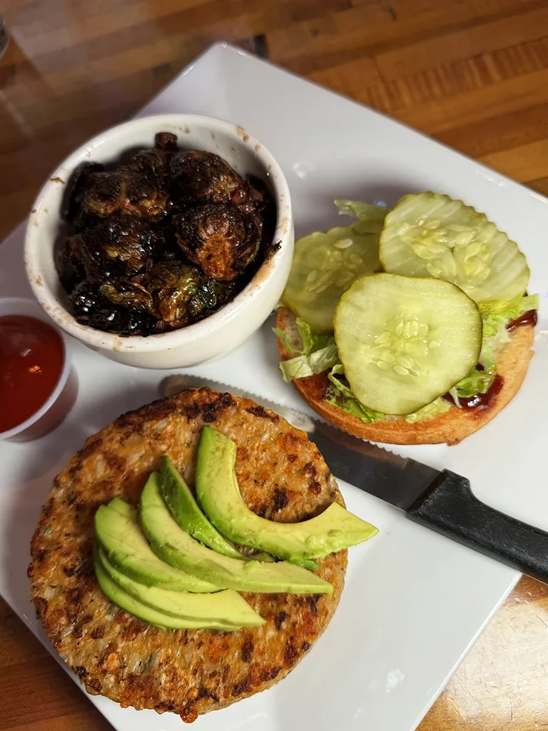 Open-faced sandwich, roasted Brussels sprouts, and ketchup on a wooden table.
