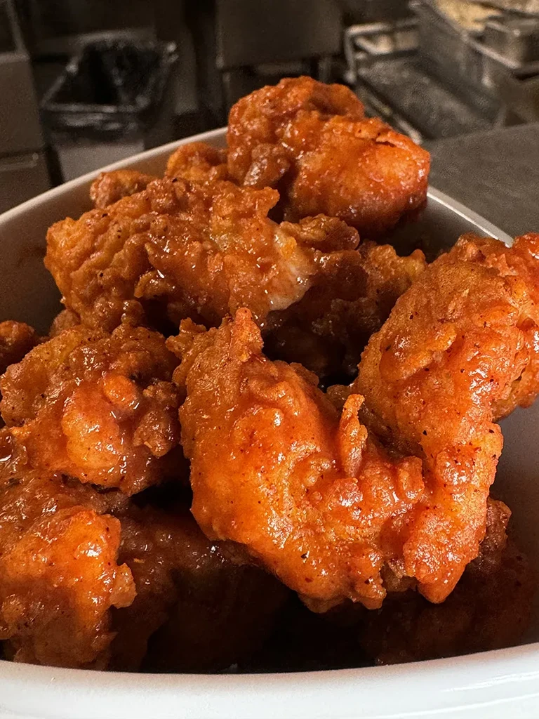 Fried chicken pieces coated in glossy reddish-orange sauce in a white bowl.